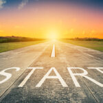 Business and beginnings concept with the word start on asphalt road. Diminishing perspective. Sun on the horizon in the distance. Colorful sunset sky. The way forward.